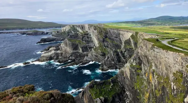 Impresionantes acantilados y el océano Atlántico azul profundo, parte de una ruta por Irlanda. Senderos serpentean por la cima verde.