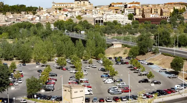 Amplio aparcamiento con muchos coches, ideal para saber donde aparcar en Toledo. Al fondo, la histórica ciudad se alza majestuosa.