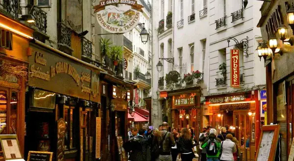 Callejuela parisina con restaurantes y gente paseando, evocando un ambiente de barrio latino en París.