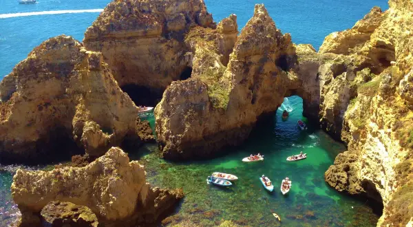¡Qué ganas de ir al Algarve en coche! Aquí, barcos exploran cuevas y arcos naturales en aguas cristalinas.