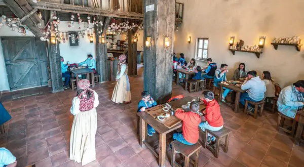 Ambiente rústico para comer en Puy du Fou. Familias y parejas disfrutan de una comida en un comedor de madera con decoración temática.