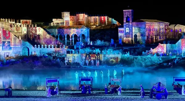 Espectáculo nocturno en Puy du Fou, Francia. Edificios históricos iluminados con proyecciones de tapices y figuras danzando en el agua.