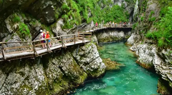 Una ruta por Eslovenia te lleva por pasarelas de madera sobre un río turquesa en un cañón verde.