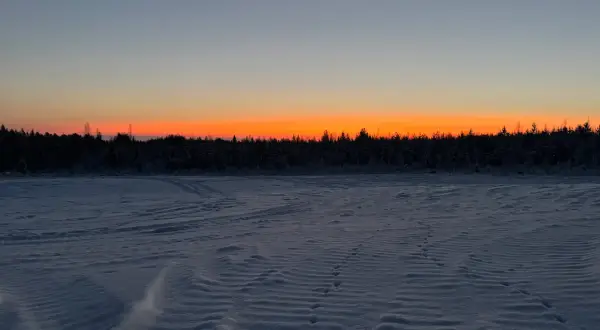 Paisaje invernal con cielo anaranjado al atardecer. Huellas en la nieve sugieren el camino para saber como ir a Laponia.