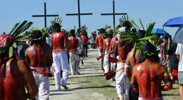 Hombres con coronas de hojas y espaldas ensangrentadas caminan hacia cruces negras, parte de una procesión de **Semana Santa Filipinas**.
