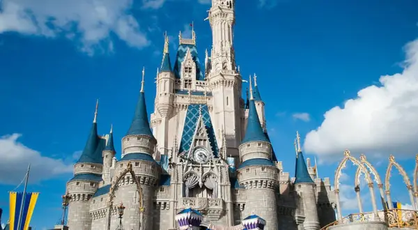 El icónico castillo de Disneyland se alza majestuoso bajo un cielo azul con nubes blancas, invitando a la magia.