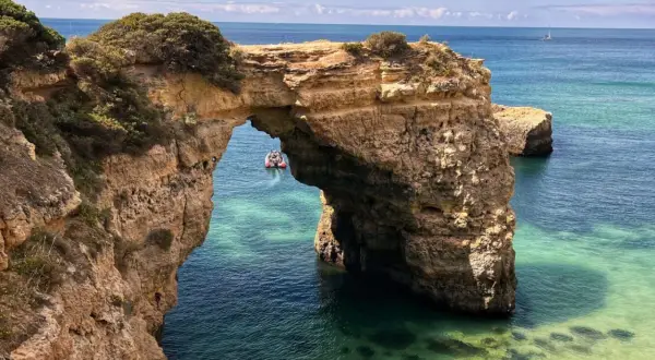 Arco natural de roca en el mar turquesa, ideal para tu plan de qué ver en Algarve en 5 días. Un bote turístico pasa por debajo.