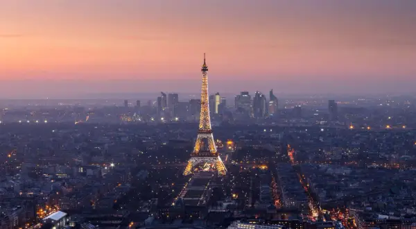 Vista panorámica de París al anochecer, con la Torre Eiffel iluminada y el horizonte de la ciudad. Un recuerdo inolvidable de las visitas a la Torre Eiffel.