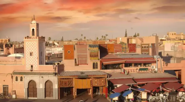 Mercado marroquí con alfombras coloridas colgadas, un minarete y tejados rojos. Consejos para viajar a Marruecos.