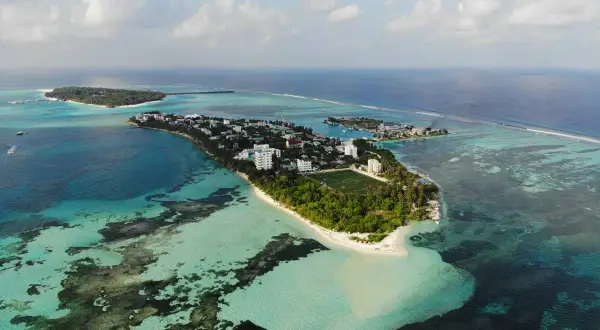 Isla con edificios, campo de fútbol y palmeras, rodeada de aguas turquesas y azules. Un sueño para viajar a Maldivas.