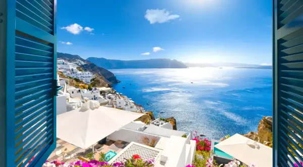 Vista de Santorini, Grecia, con casas blancas en la ladera y el mar azul brillante. ¡Un lugar perfecto donde viajar en junio!