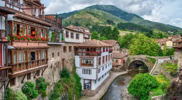 Encantadores pueblos costeros de Cantabria con casas de madera y piedra, balcones floridos y un río serpenteante bajo un puente antiguo.