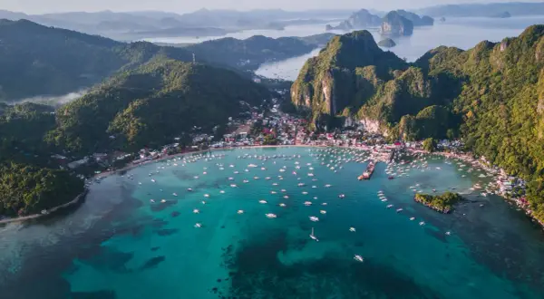 Vista aérea de El Nido, Filipinas. Un mar turquesa lleno de barcos, con una costa verde y montañosa. ¡Perfecto para tu próxima aventura con una tarjeta SIM Filipinas!
