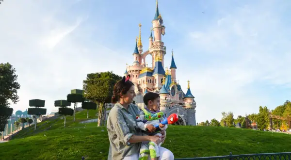 Madre e hijo disfrutan de un día mágico en Disneyland París. El niño, vestido de Buzz Lightyear, sostiene un juguete mientras admiran el castillo.
