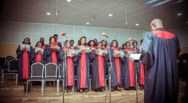 Coro cantando en una misa gospel en Nueva York, con túnicas azules y rojas, leyendo partituras.