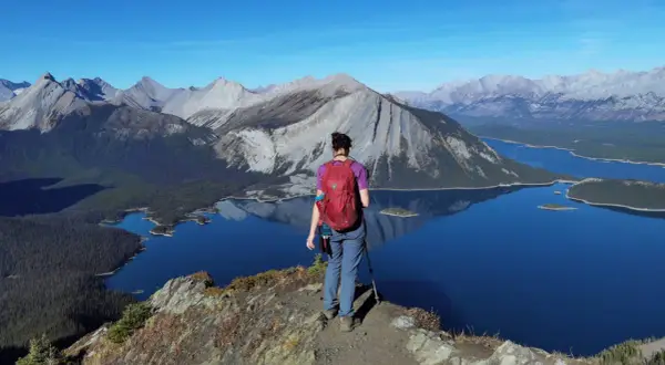 Senderista admira el paisaje montañoso y lagos turquesas, un ejemplo de qué ver en Canadá.