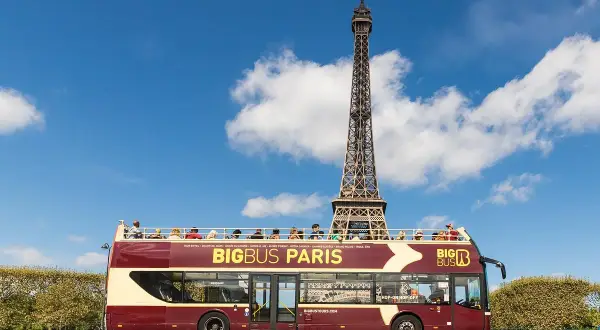 Autobús turístico Big Bus Paris con la Torre Eiffel de fondo. Turistas disfrutan del viaje en la cubierta superior.