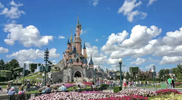 El castillo rosa de Disneyland Paris, rodeado de flores y gente, es el centro de sus atracciones.