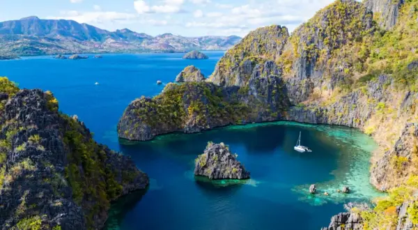 Un velero navega en aguas turquesas rodeado de acantilados verdes y rocosos en Filipinas en octubre.