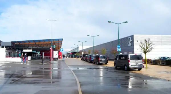 Llegando a **París Beauvais al centro**, taxis esperan bajo un cielo nublado. El aeropuerto tiene una zona de embarque y un edificio largo con el número 2.