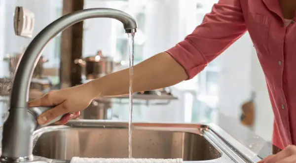 Mano abre grifo en cocina. El agua fluye, demostrando que el agua de París es potable y segura para beber.