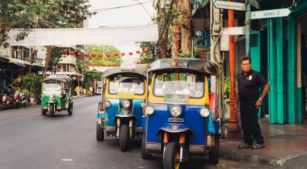 Tuk-tuks coloridos esperan en una calle de Bangkok. Un hombre observa. ¡La mejor época para viajar a Tailandia es ahora!