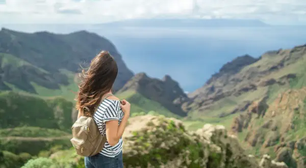 Mujer con mochila admira el paisaje montañoso y el mar, imaginando el viaje en barco Tenerife La Gomera.