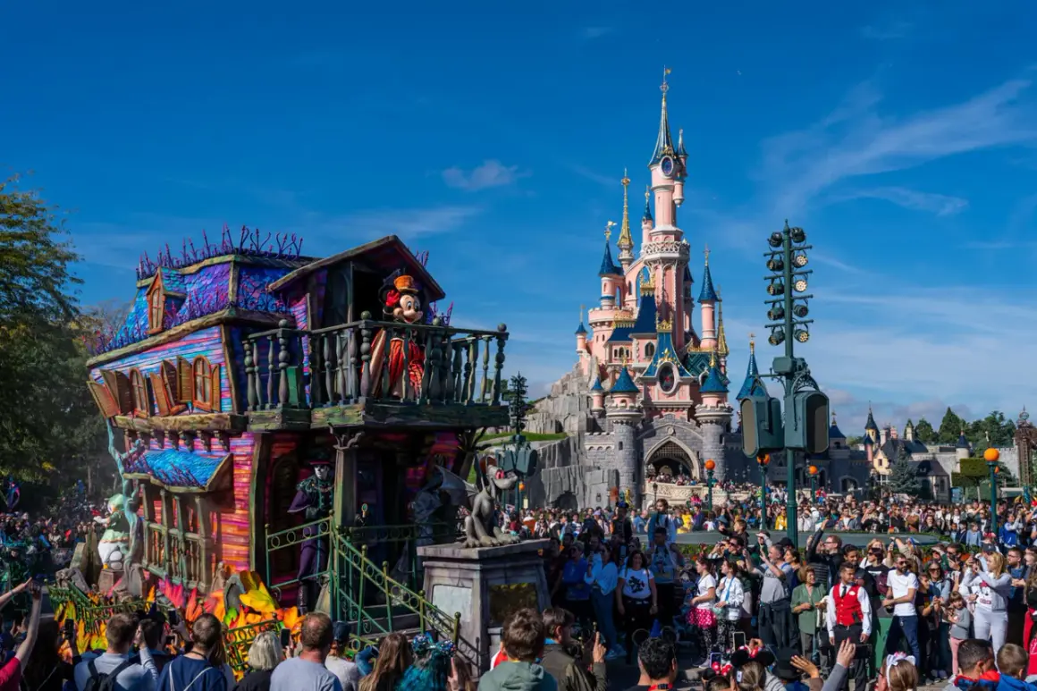 Desfile de **Disneyland Paris Halloween** con Mickey Mouse en un carro espeluznante frente al castillo.