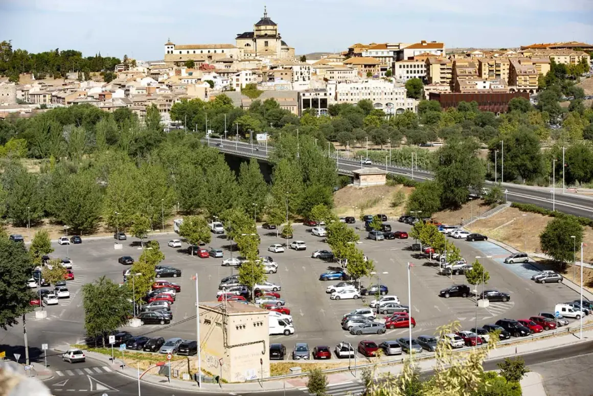 Amplio aparcamiento con muchos coches, ideal para saber donde aparcar en Toledo. Al fondo, la histórica ciudad se alza majestuosa.