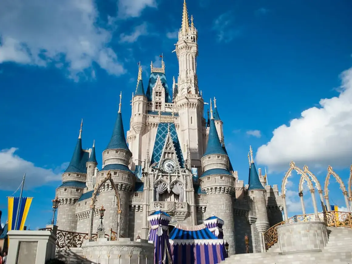 El icónico castillo de Disneyland se alza majestuoso bajo un cielo azul con nubes blancas, invitando a la magia.