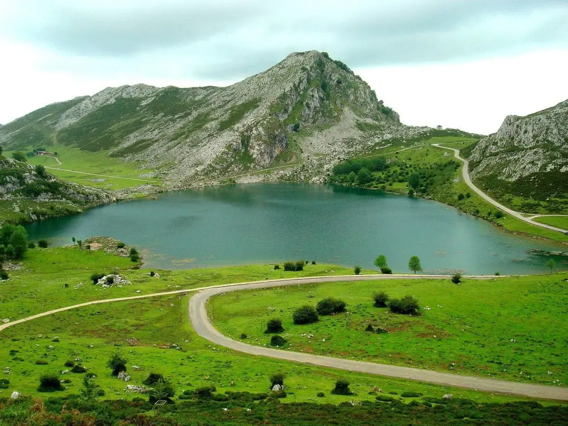 Lago en Cangas de Onís que ver: un paisaje montañoso verde con un lago sereno y carreteras serpenteantes.