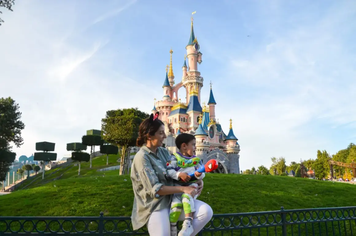 Madre e hijo disfrutan de un día mágico en Disneyland París. El niño, vestido de Buzz Lightyear, sostiene un juguete mientras admiran el castillo.
