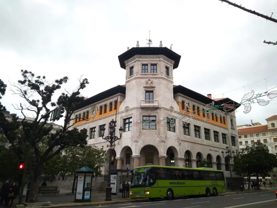 Autobús verde de ALSA en la calle, frente a un edificio histórico. Un buen lugar para aparcar en Santander y disfrutar de la arquitectura.