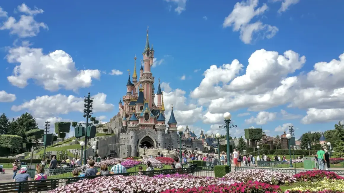 El castillo rosa de Disneyland Paris, rodeado de flores y gente, es el centro de sus atracciones.