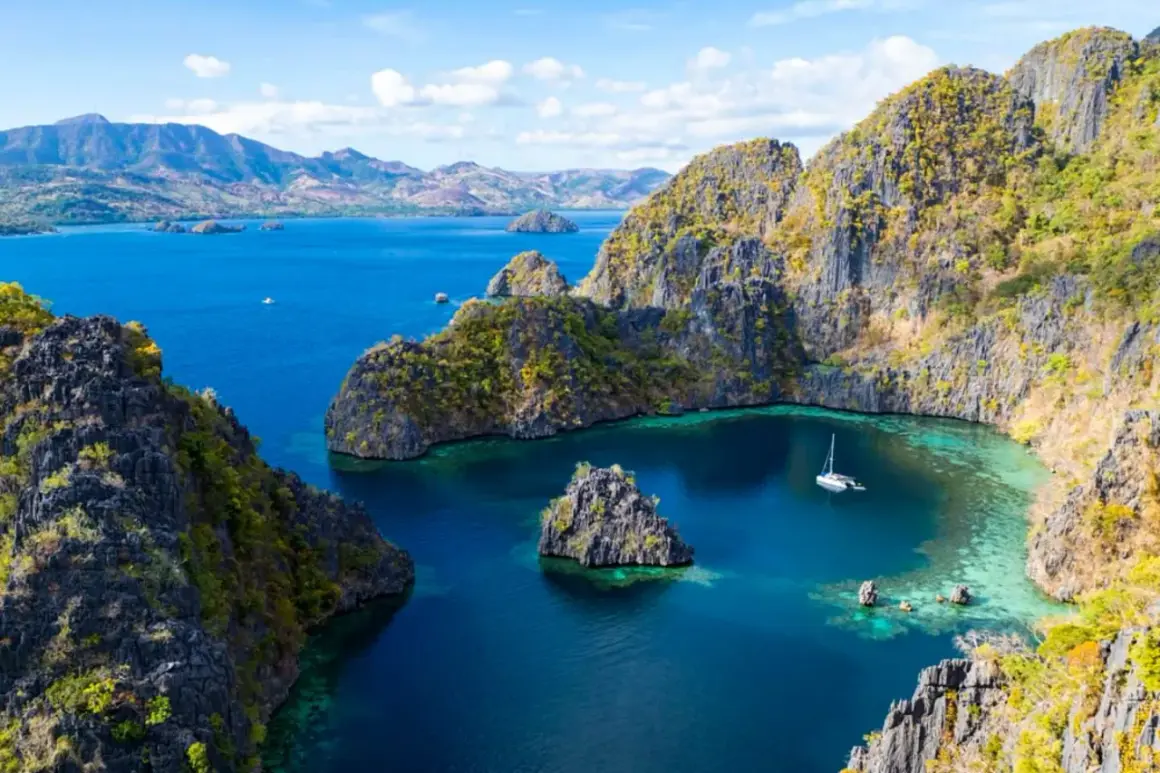 Un velero navega en aguas turquesas rodeado de acantilados verdes y rocosos en Filipinas en octubre.