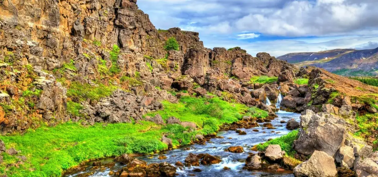 Río serpenteante entre rocas y hierba verde en el Parque Nacional Thingvellir, Islandia. Cascadas pequeñas caen en el agua.