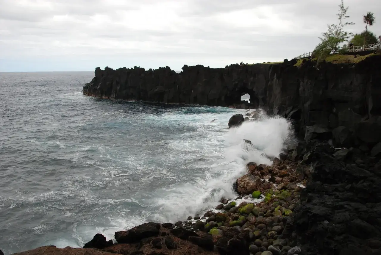 Costa rocosa de la isla Reunión, con olas rompiendo contra las rocas. El mar agitado y los acantilados imponentes sugieren los peligros de esta isla.