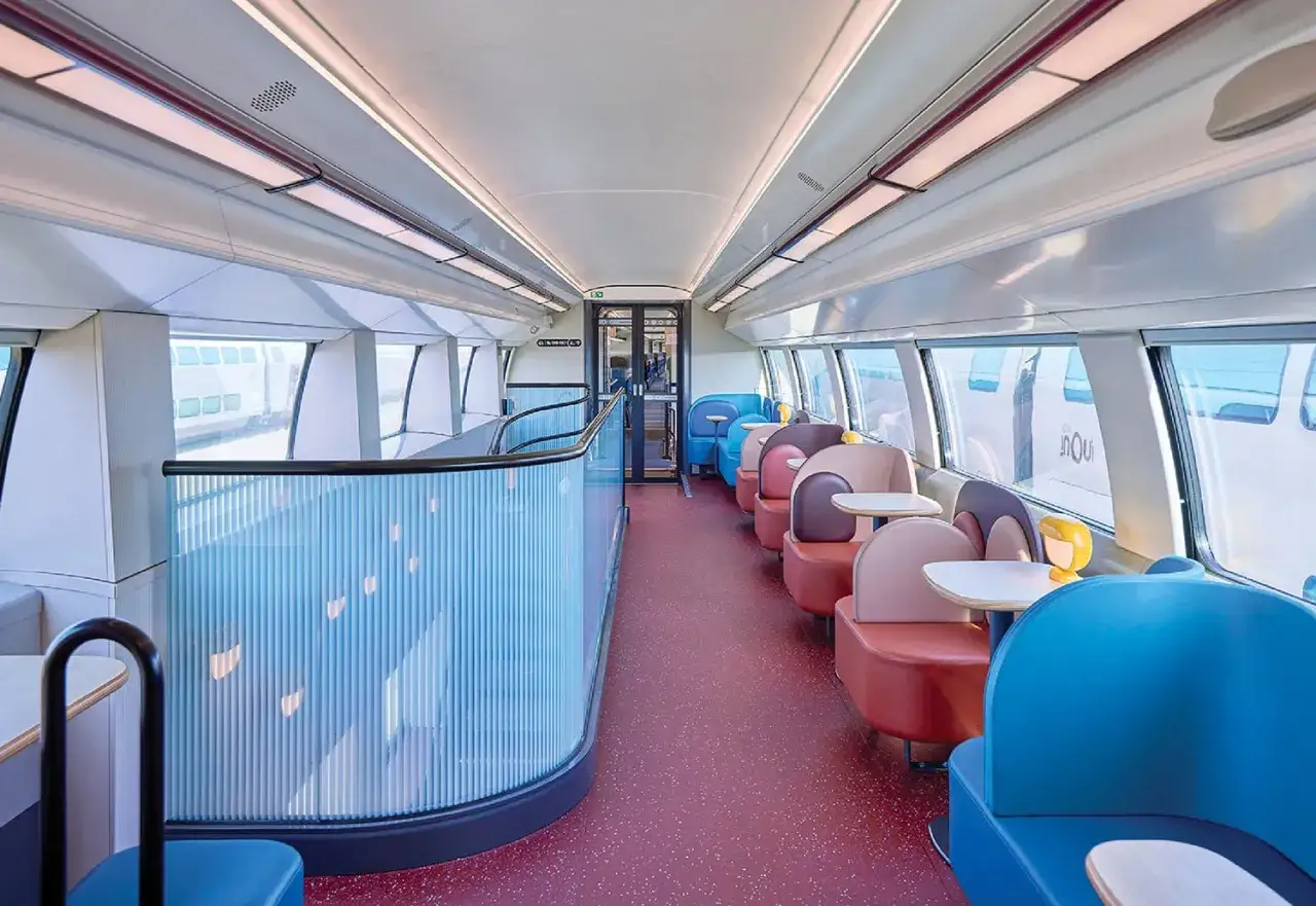 Interior de un moderno tren de Roma a Florencia con asientos coloridos y una barandilla de cristal.