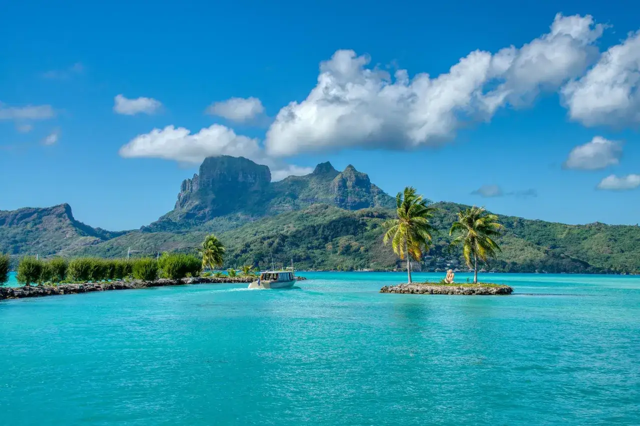 Un bote navega en aguas turquesas, con palmeras y monta&ntilde;as verdes. Un destino ideal para saber donde viajar en agosto.