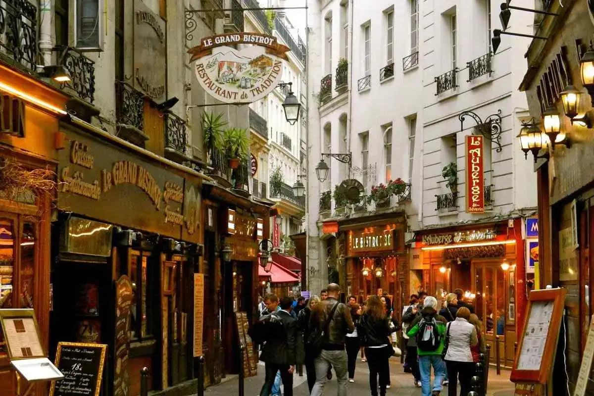 Un callej&oacute;n con restaurantes y gente paseando, evocando la atm&oacute;sfera de un barrio latino en Par&iacute;s.