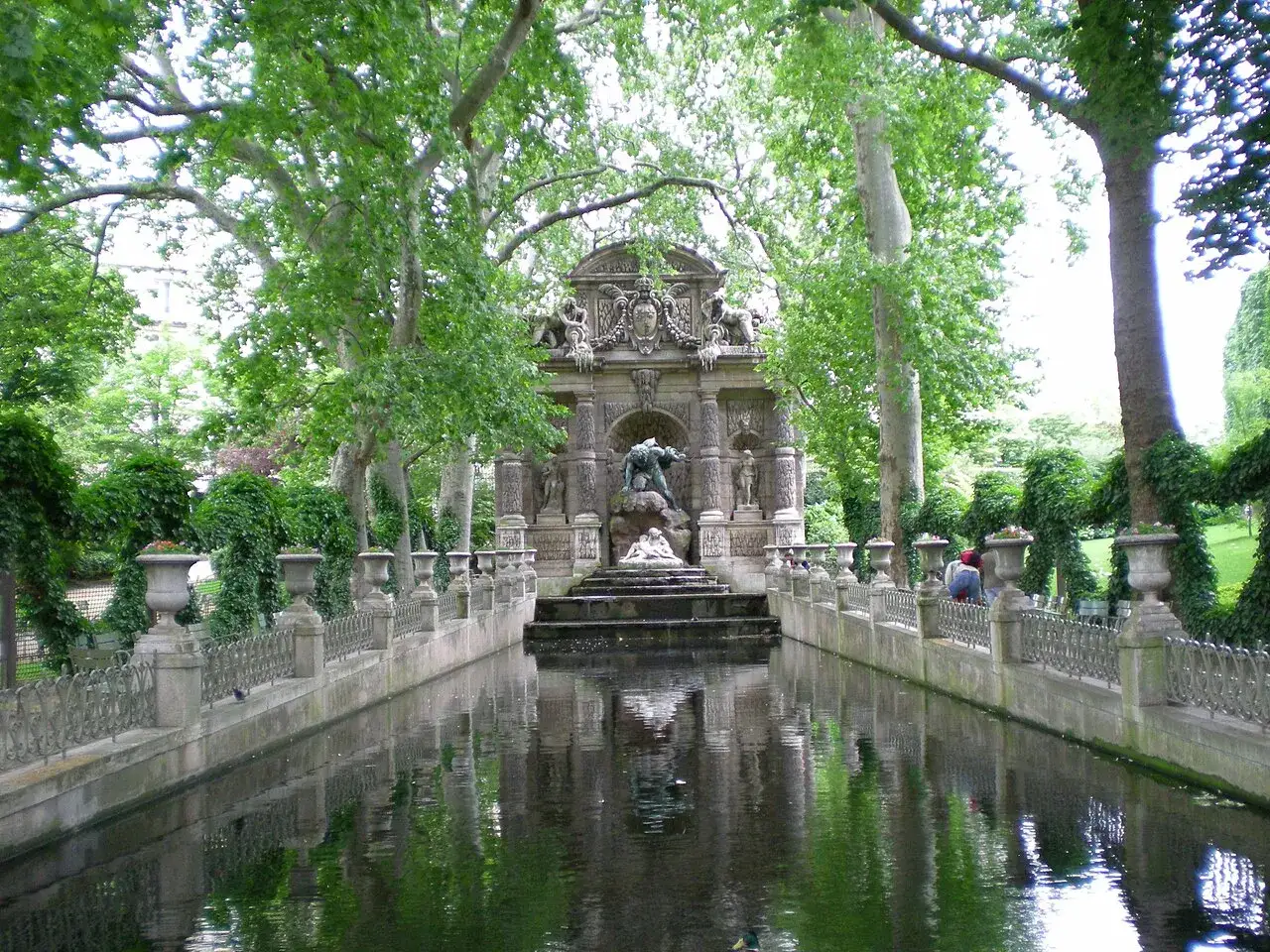 Estanque sereno en los jardines de Luxemburgo, con una fuente monumental y árboles frondosos.