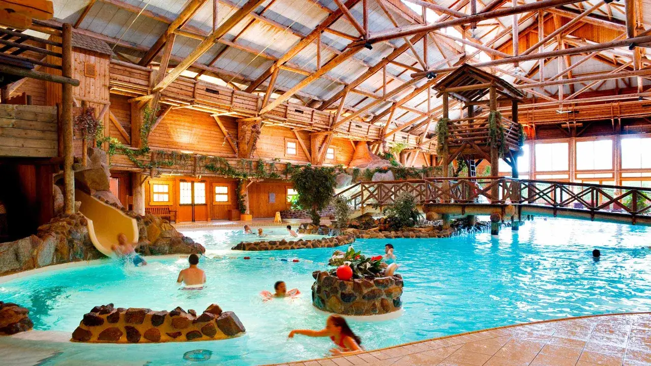 Diversi&oacute;n acu&aacute;tica en el Davy Crockett Ranch, con tobog&aacute;n, piscina y un puente r&uacute;stico bajo un techo de madera.
