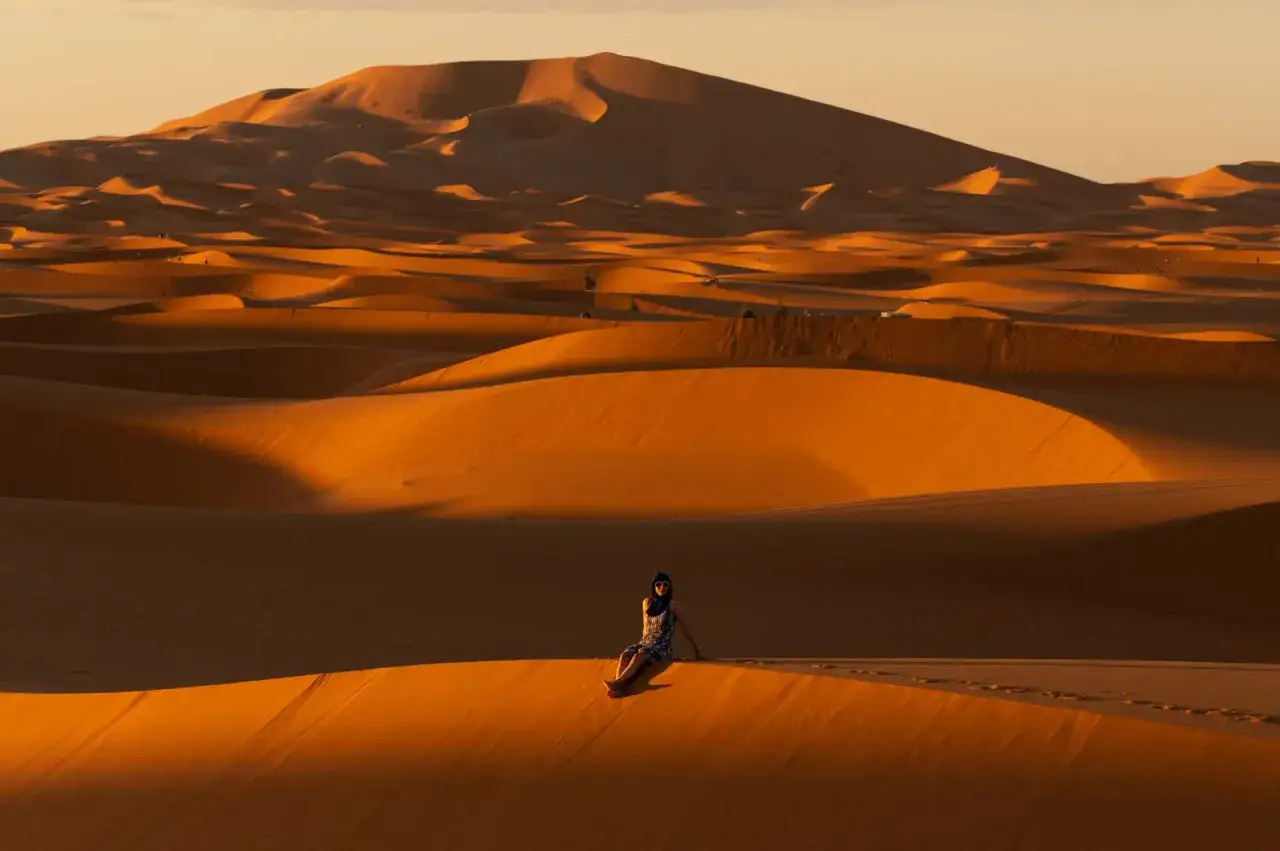 Una persona descansa en las dunas doradas del desierto, un paisaje que evoca el viaje de marrakech a merzouga.