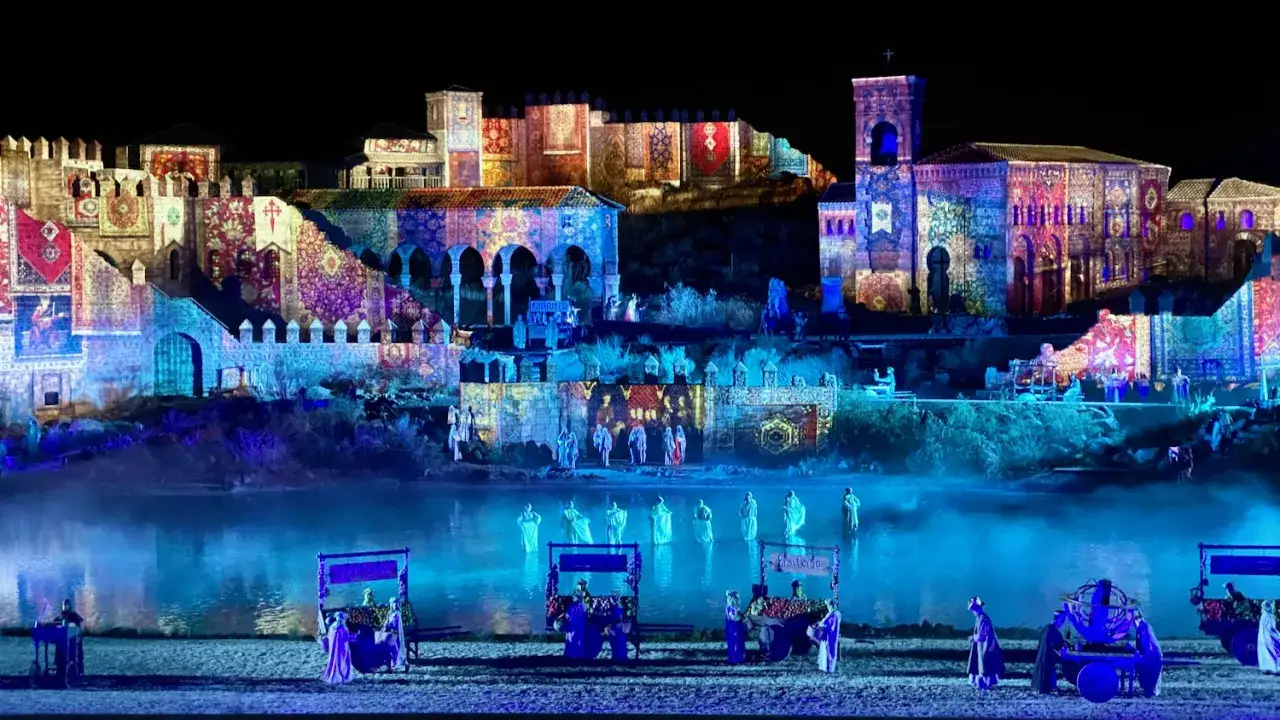 Espectáculo nocturno en Puy du Fou Toledo, con proyecciones de alfombras y figuras históricas sobre edificios y un lago con actores.
