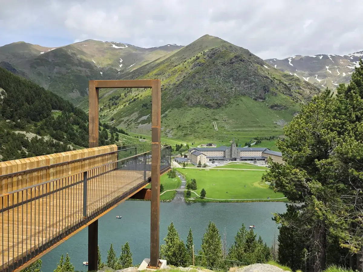 Mirador moderno sobre el lago en Vall de N&uacute;ria, ideal para explorar las rutas Vall de Nuria. Monta&ntilde;as verdes y un santuario al fondo.