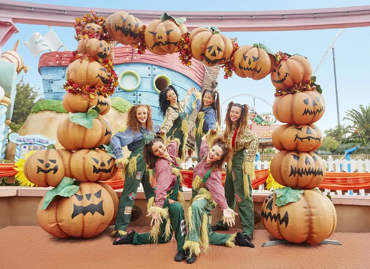 Animadoras con disfraces de espantap&aacute;jaros posan junto a calabazas gigantes en PortAventura Halloween.
