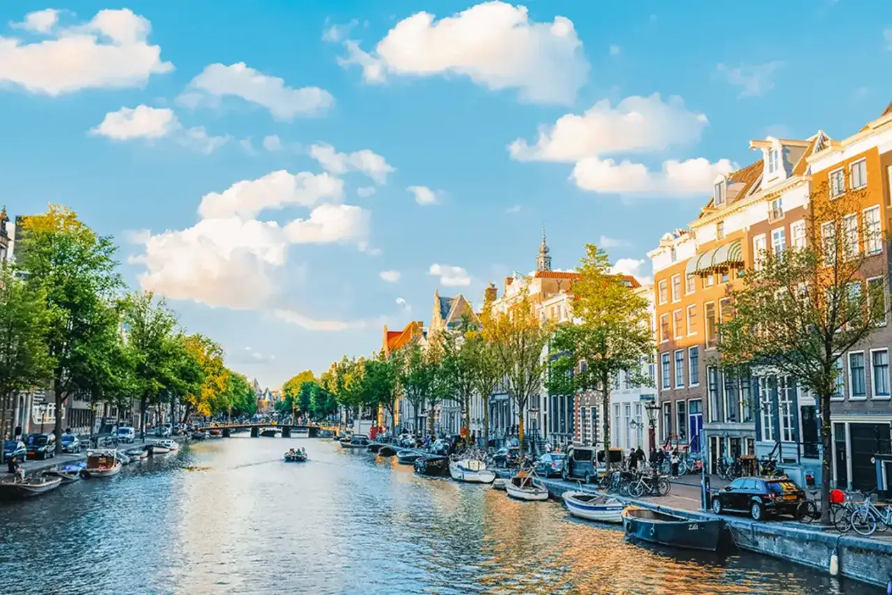 Un canal de &Aacute;msterdam con barcos, casas hist&oacute;ricas y &aacute;rboles frondosos. &iexcl;Perfecto para planificar qu&eacute; hacer en &Aacute;msterdam en 3 d&iacute;as!