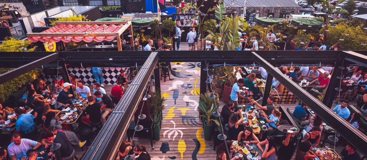 Gente disfrutando en una terraza con decoraci&oacute;n que evoca cosas t&iacute;picas de Francia, como banderas y toldos a rayas.
