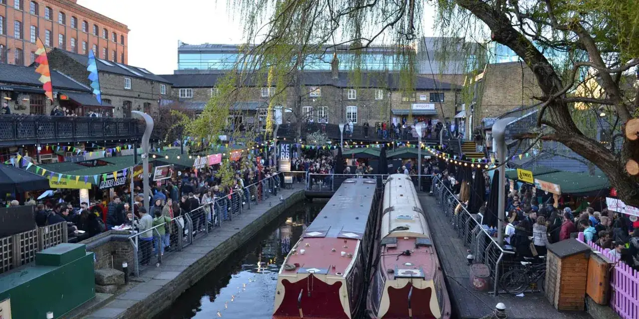 Mercado bullicioso con puestos de comida, barcos en el canal y gente disfrutando de cosas t&iacute;picas de Londres.