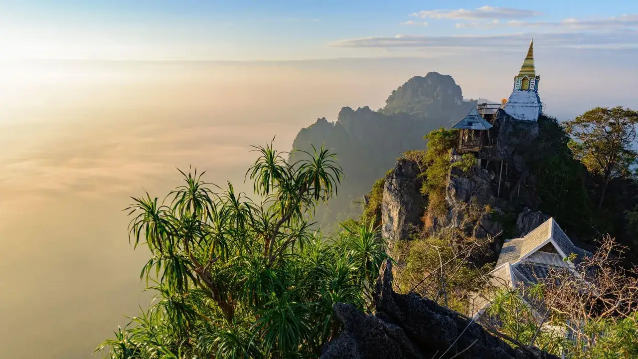 Templo dorado en la cima de una montaña rocosa, con un mar de nubes al amanecer en Mae Hong Son.